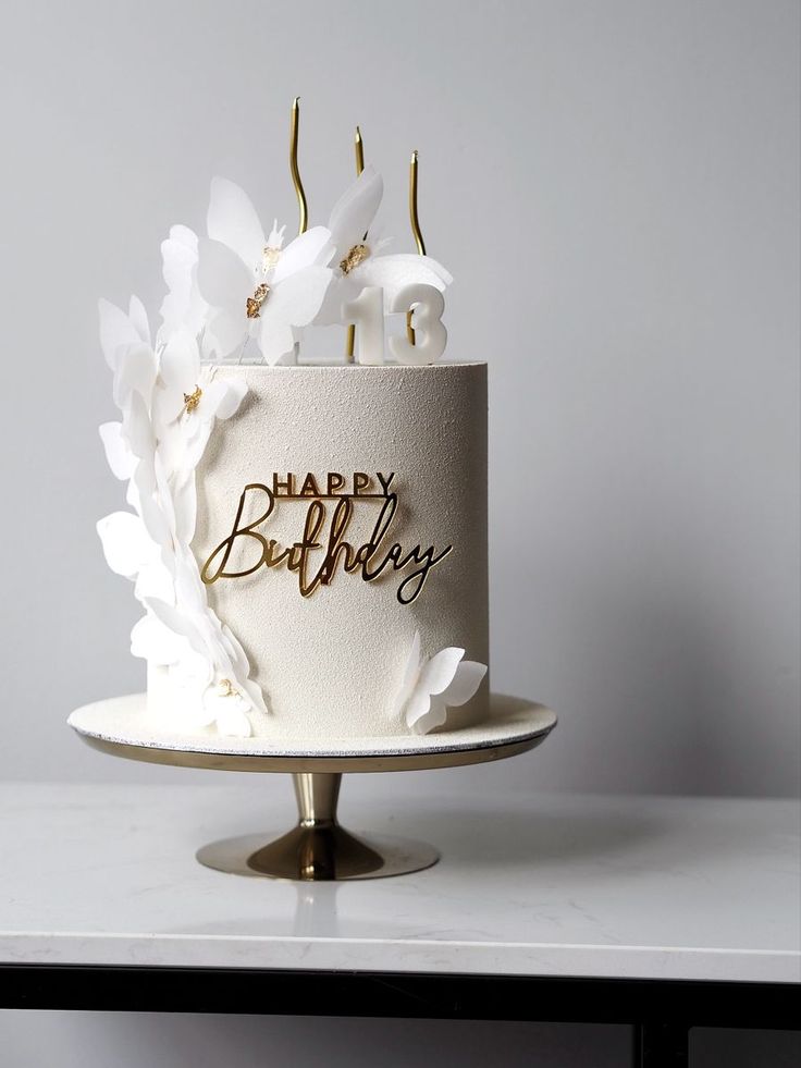 a birthday cake with white flowers and gold lettering on the top that says happy birthday