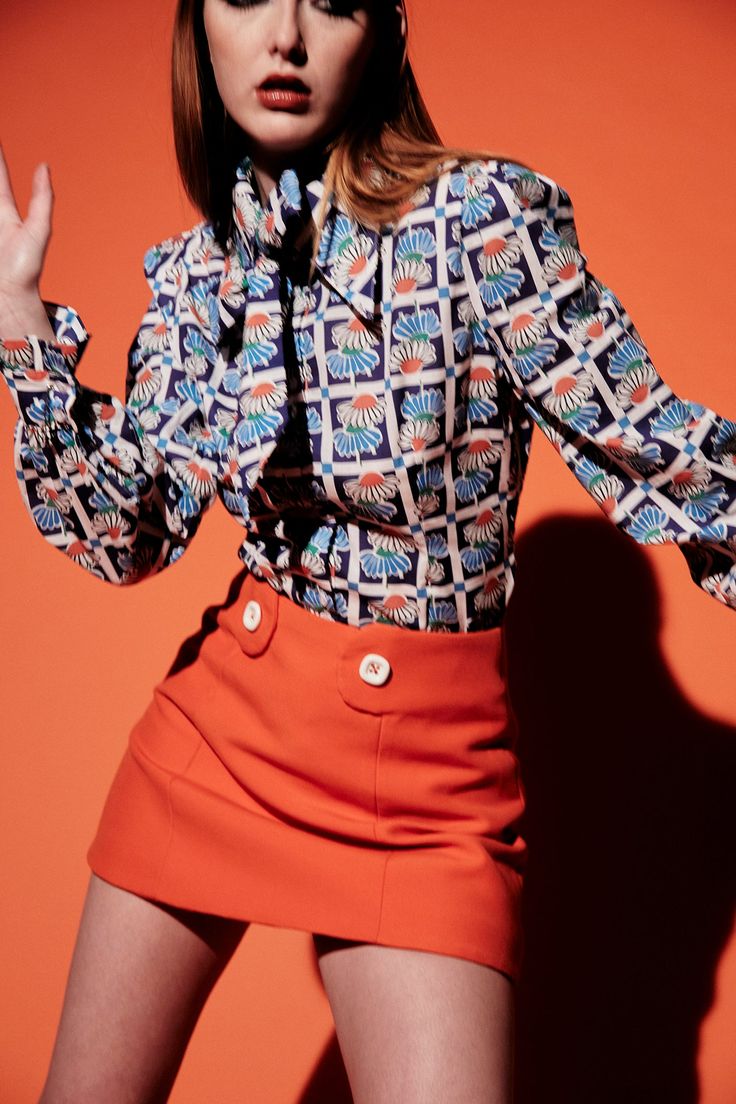 a woman in an orange skirt posing with her hands on her hips and wearing a patterned shirt