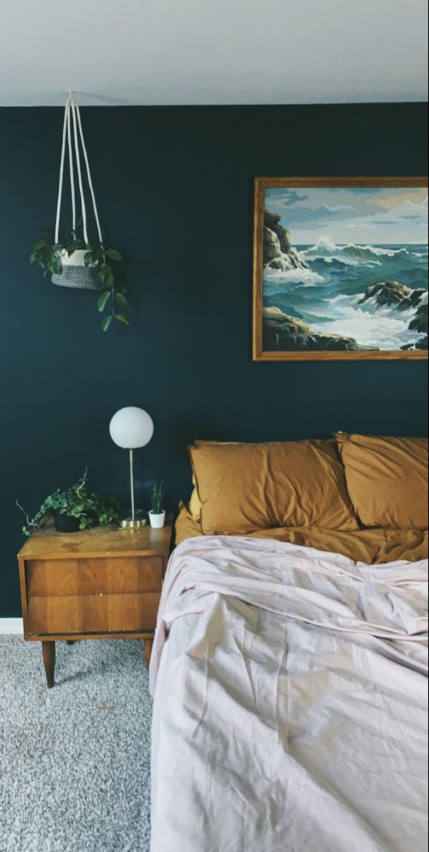 a bedroom with a bed, nightstand and painting on the wall above it that is dark blue