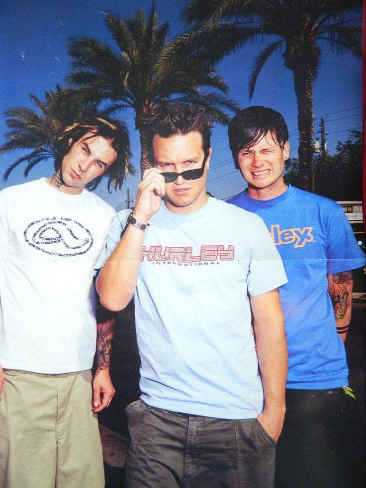 three men standing next to each other with palm trees in the background and one man talking on his cell phone