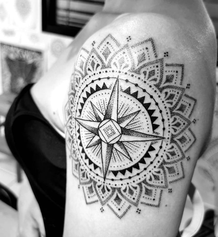 a black and white photo of a woman's shoulder with a compass tattoo on it