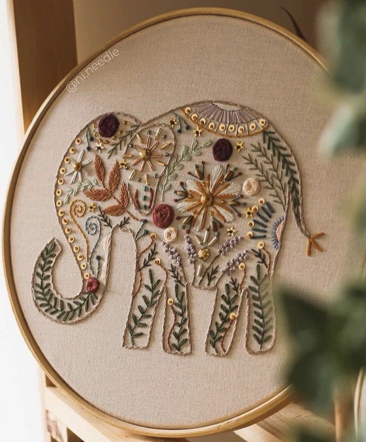 an elephant with flowers and leaves on it's back is embroidered onto a wooden frame