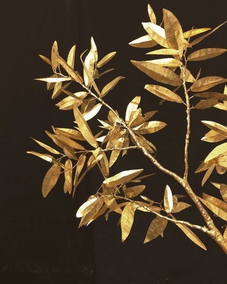 a branch with yellow leaves on it against a black background that is partially covered in gold foil