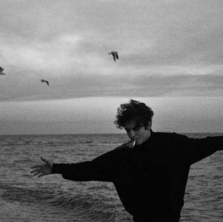 a man standing on top of a beach next to the ocean holding his arms out