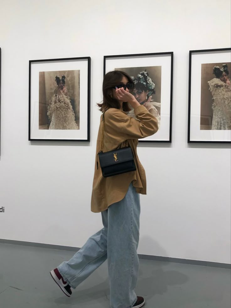 a woman walking in front of pictures on the wall with her hand to her face