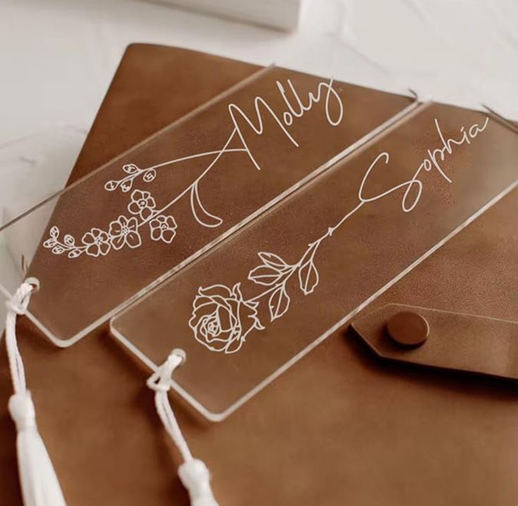 two clear acrylic signs with flowers on them sitting on a brown leather bag