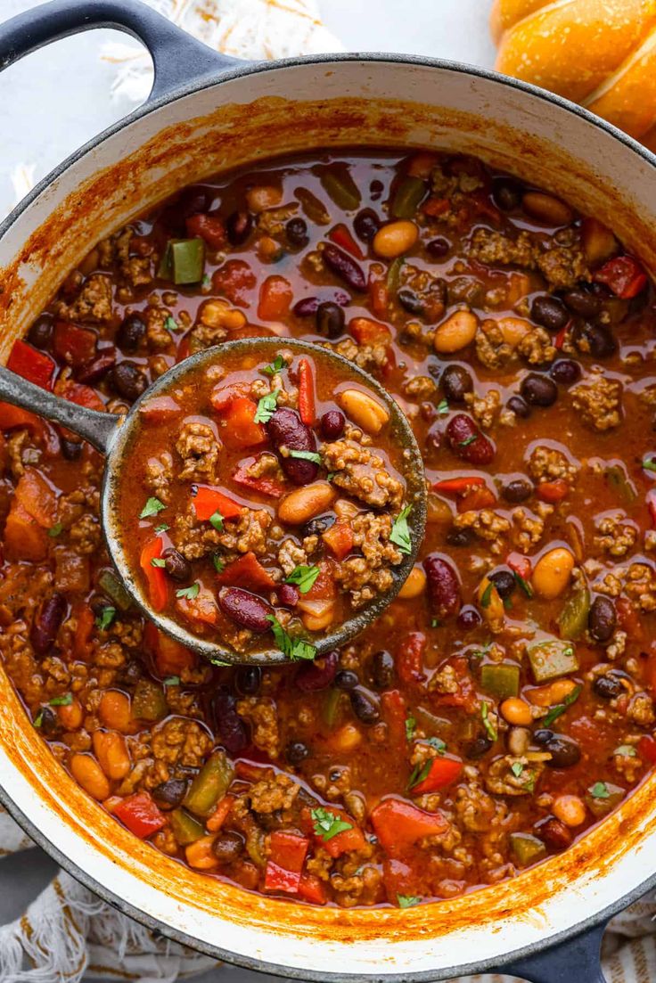 a ladle full of chili and beans in a pot with bread on the side