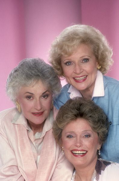 three women are posing for a photo in front of a pink background and one is holding her arm around the other woman's shoulder