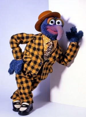 a stuffed animal dressed in a checkered suit and hat leaning against a white wall