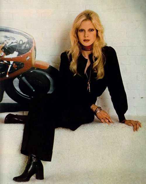 a woman sitting on top of a white surface next to a motorcycle helmet and motorbike