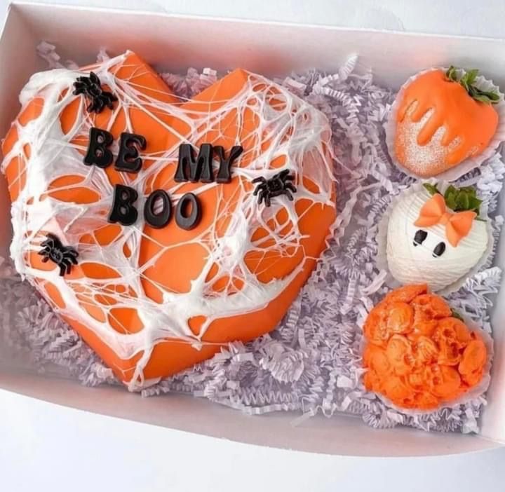 an orange heart shaped cake with white frosting in a box next to other treats