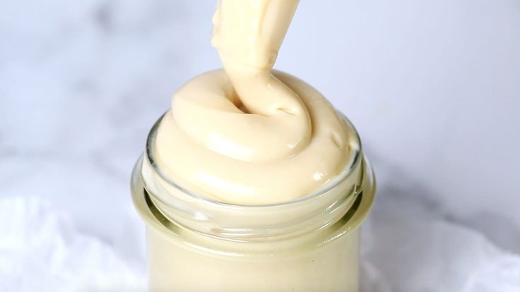 a jar filled with cream sitting on top of a white tablecloth next to a spoon