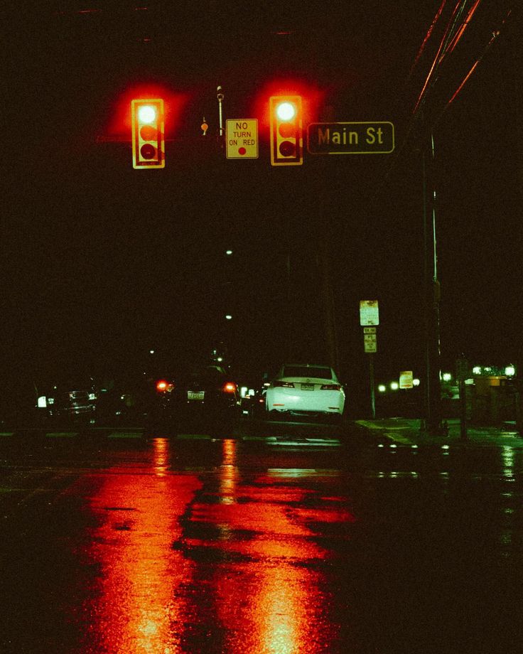 two red traffic lights above a wet street at night with cars driving on the road