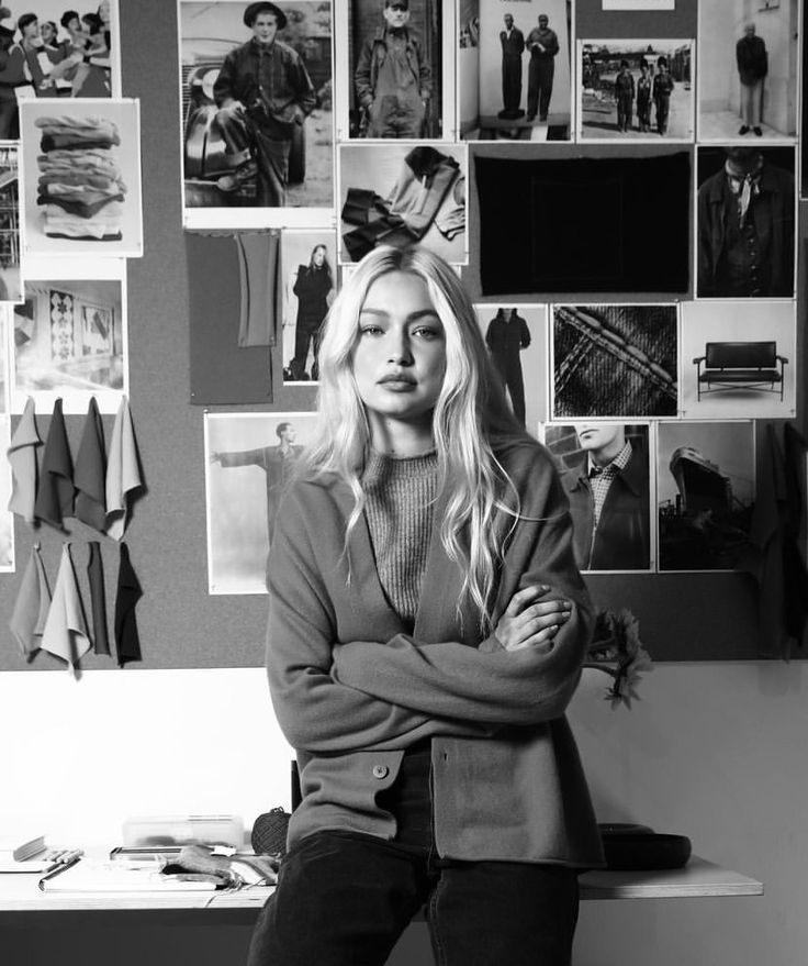 a woman sitting on top of a desk next to a wall covered in pictures and photos