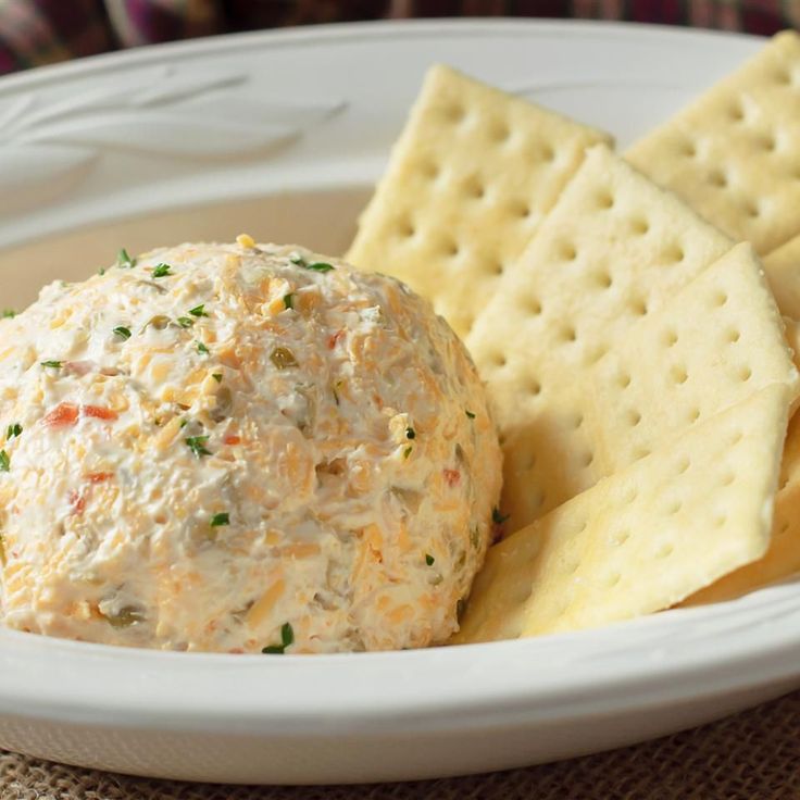 a white plate topped with crackers and cheese ball next to crackers on a table