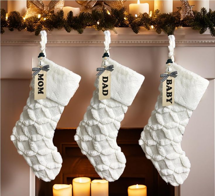 two white christmas stockings hanging from a mantel with candles in front of them and a fireplace