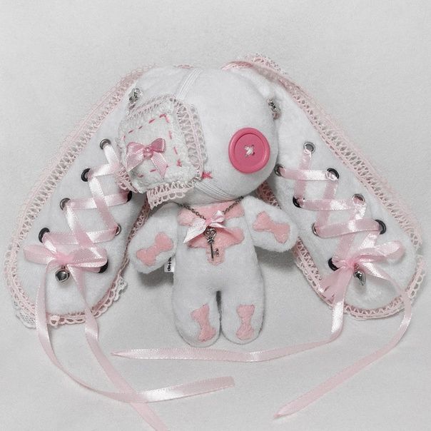 a white teddy bear with pink bows on it's head sitting next to a ribbon