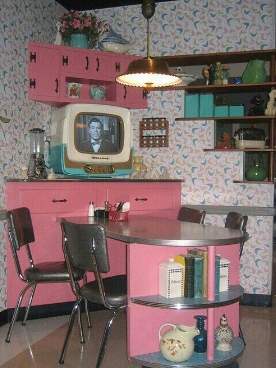 an old fashioned kitchen with pink cabinets and chairs in front of a tv on the wall