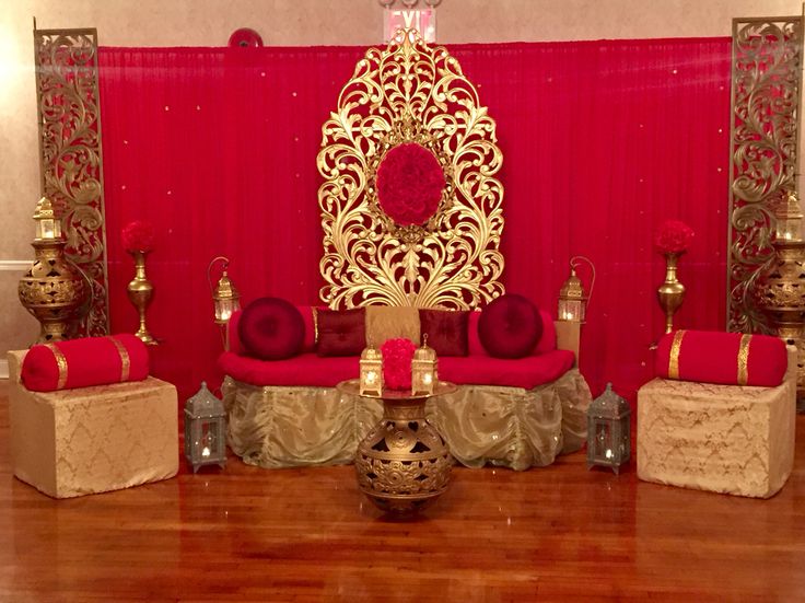 a red and gold wedding set up with chairs, vases and candles on the floor