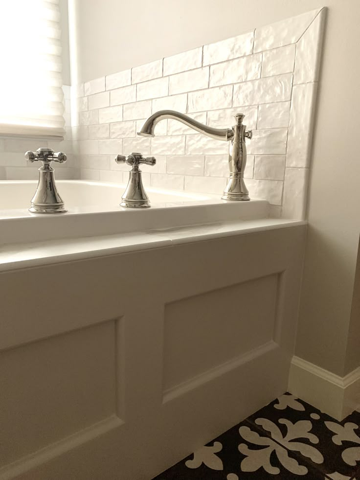 two faucets sitting on top of a white sink next to a black and white tile floor