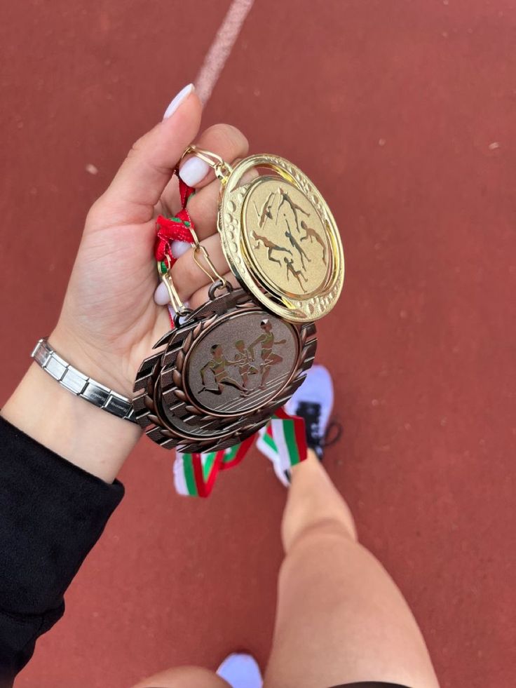 a woman holding two medals in her hand on top of a tennis court with red and white stripes