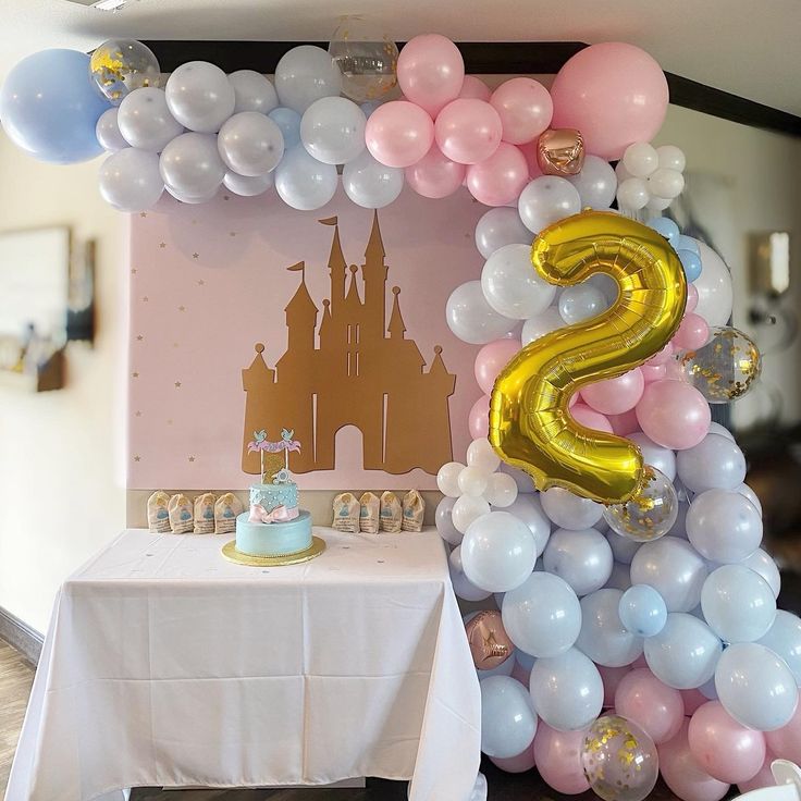 a table with a cake and balloons on it in front of a castle balloon wall