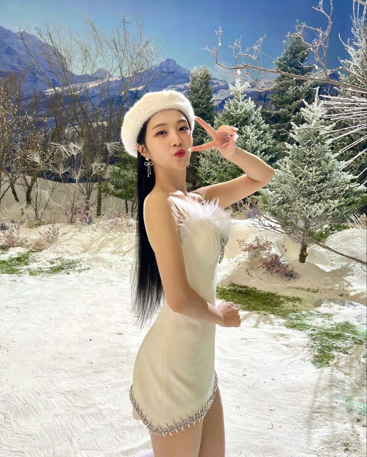 a woman in a white dress and hat posing for the camera with snow on the ground behind her