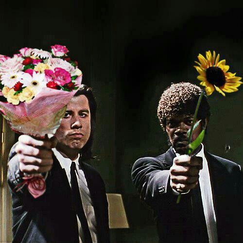 two men in suits are holding flowers and pointing at the same person with one hand