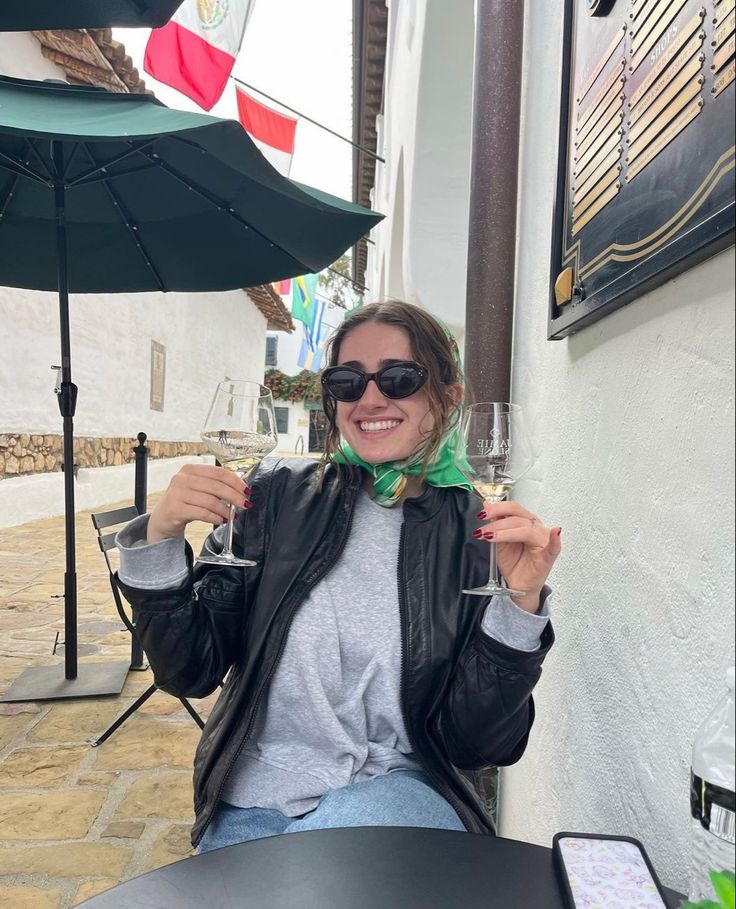 a woman sitting at a table with a glass of wine in her hand and an umbrella over her head