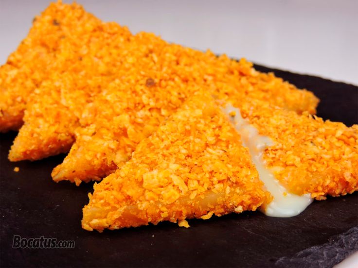 two pieces of fried chicken on a black plate with white sauce and parmesan cheese