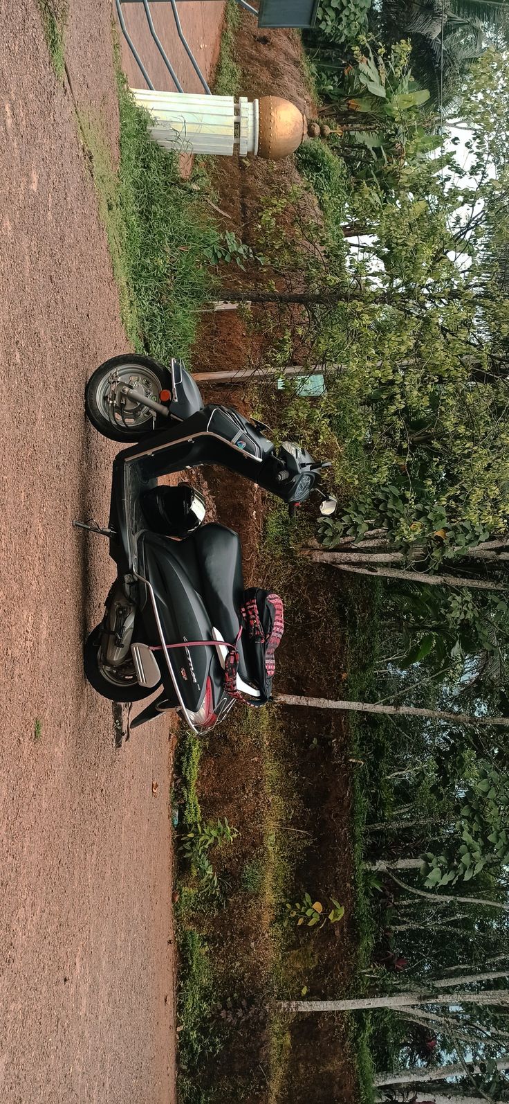 a motor scooter parked on the side of a dirt road next to trees