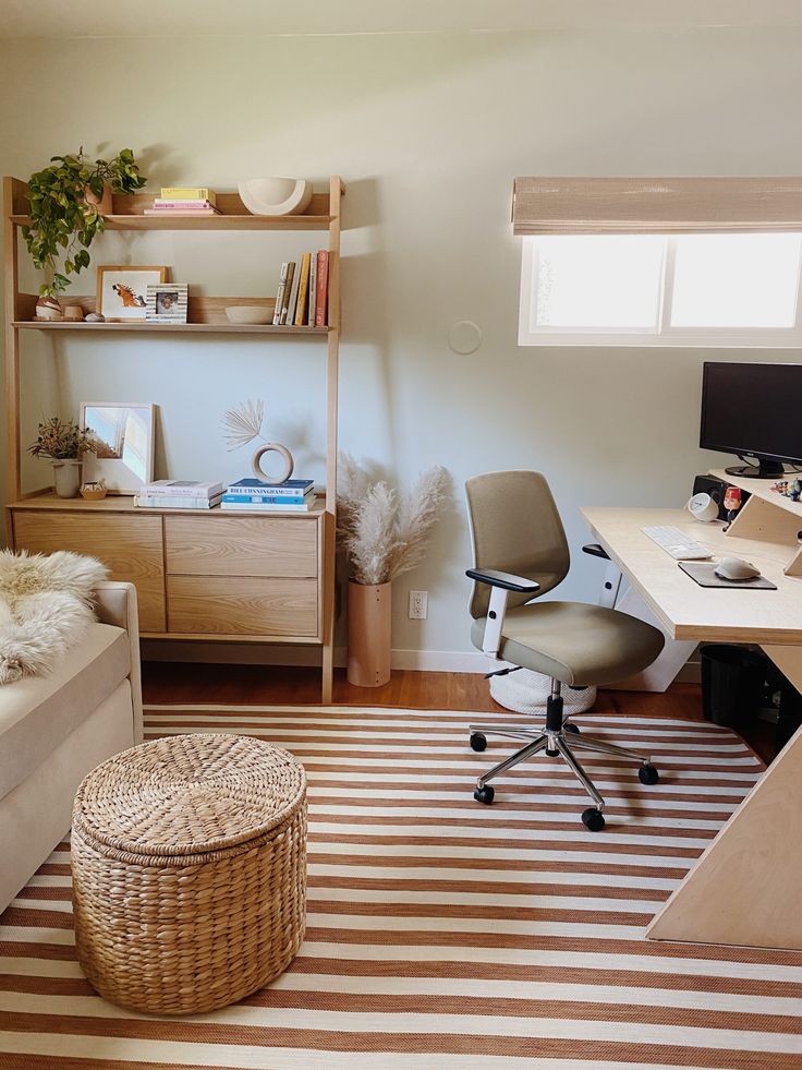 a room with a desk, chair and computer on top of a striped rug in front of a window