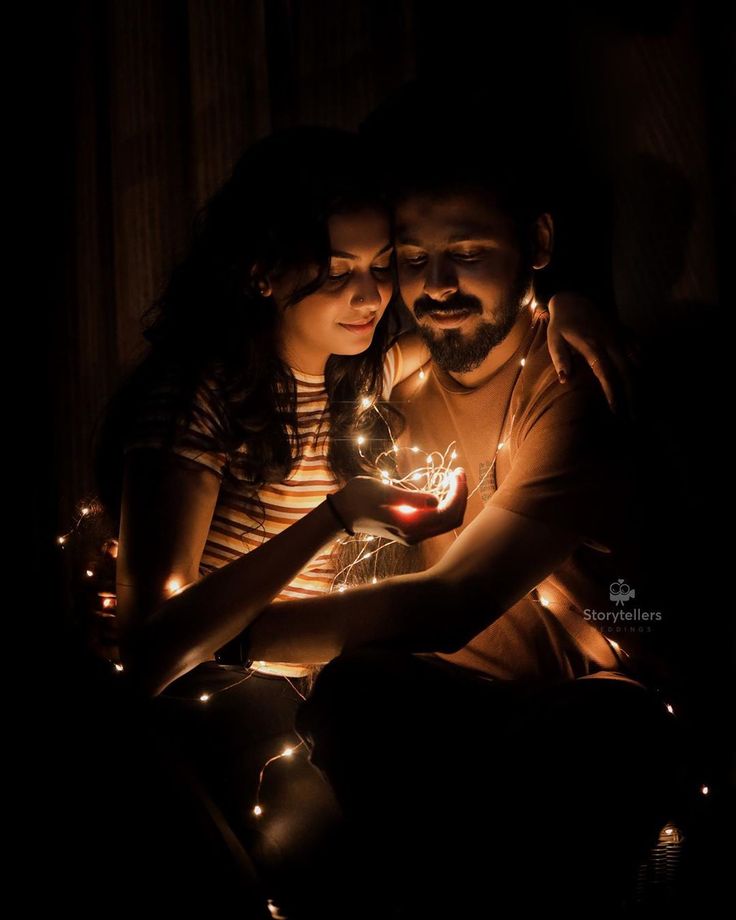 a man and woman sitting next to each other in the dark holding a lit candle