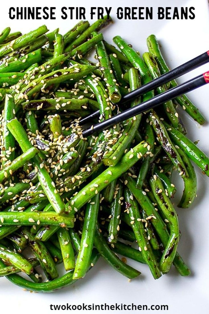 a white plate topped with green beans covered in sesame seeds and seasoning next to chopsticks