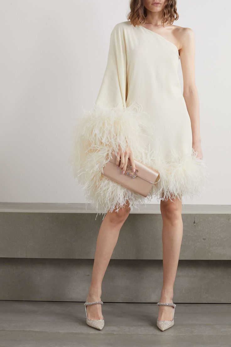 a woman in a white dress with feathers on the skirt and one hand holding a pink purse