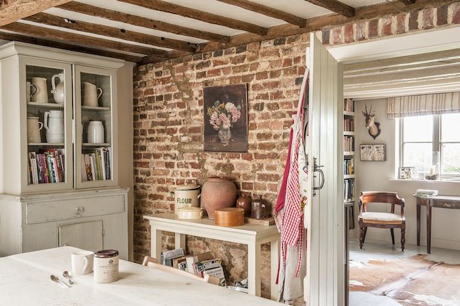 an old brick wall in a kitchen with white counter tops and cabinets, next to a dining room table