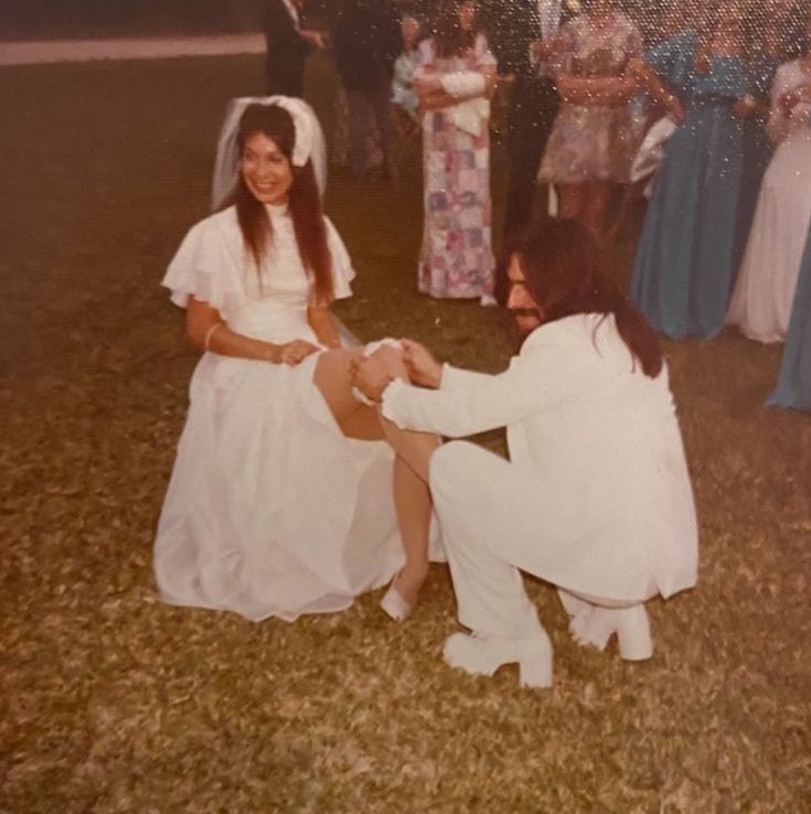 an old photo of two women dressed in white kneeling down on the ground with other people standing behind them