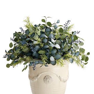 a white vase filled with lots of green plants