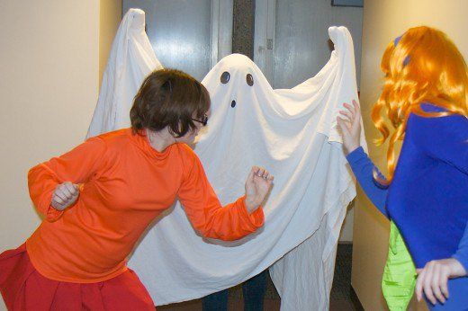 two people dressed in halloween costumes standing next to each other with ghost curtains behind them