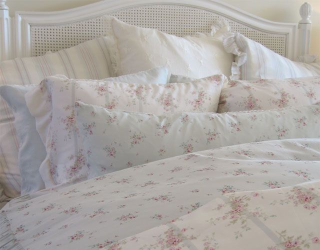 a bed with white sheets and pink flowers on it's headboard is shown