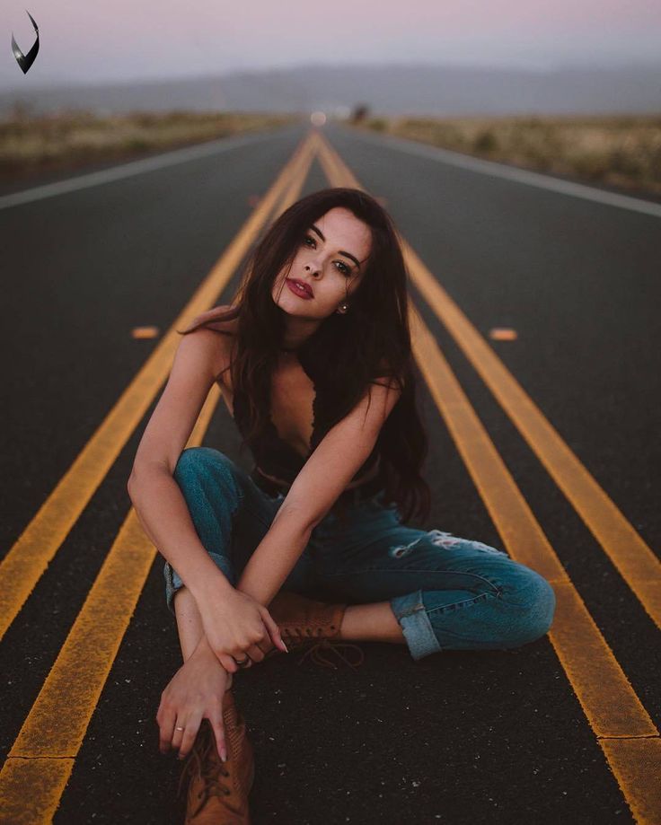 a woman sitting on the side of an empty road