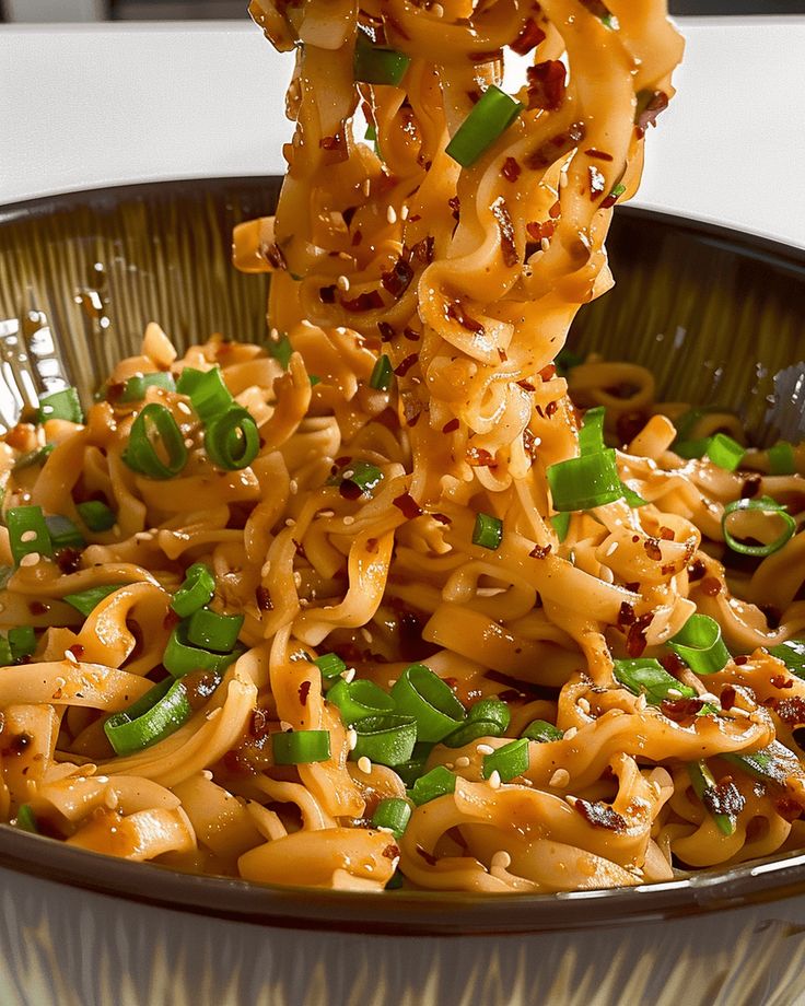 a spoon full of noodles with green onions and seasoning being lifted from the bowl