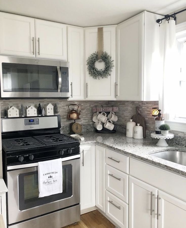 a kitchen with white cabinets and stainless steel stove top oven in the center, surrounded by wreaths on the wall