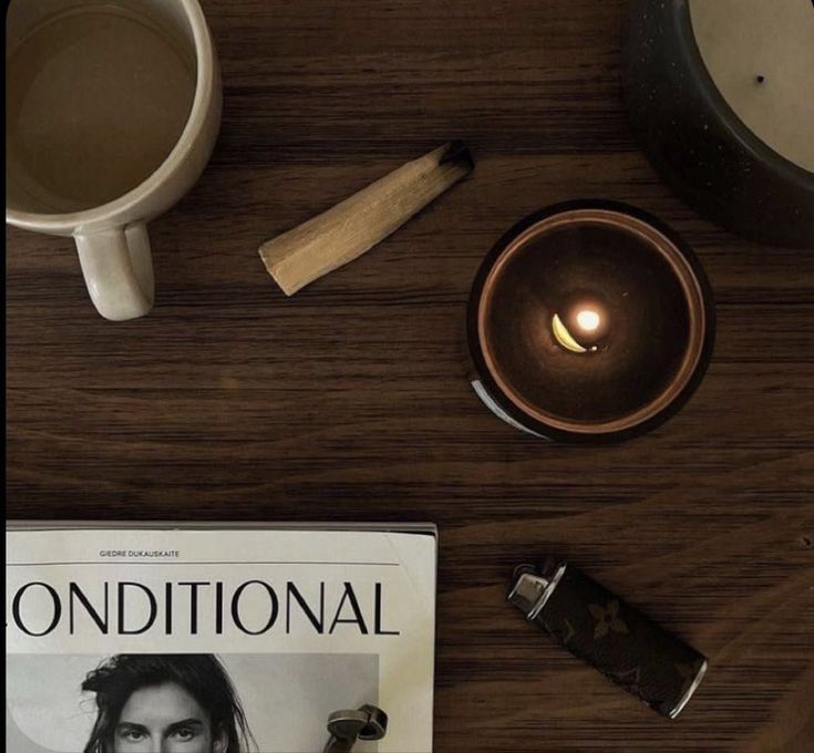 a table with a magazine, candle and cup of coffee next to it on top of a wooden table