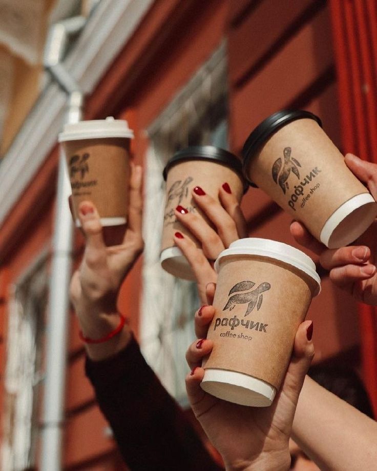 several people holding up coffee cups in front of a building