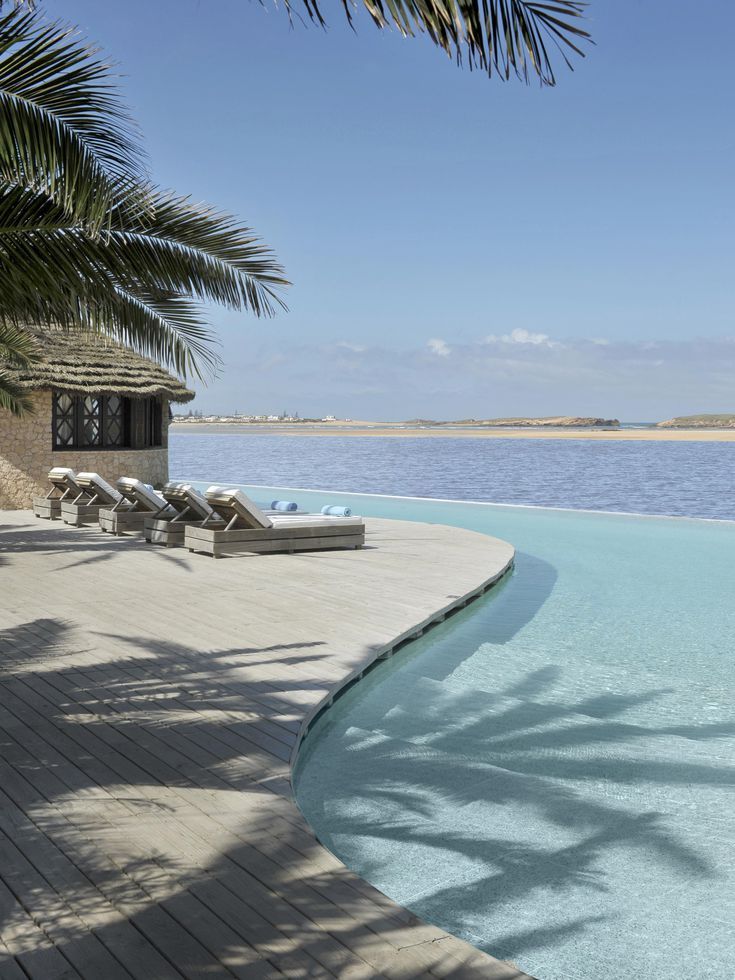 an empty swimming pool with chaise lounges next to the water's edge