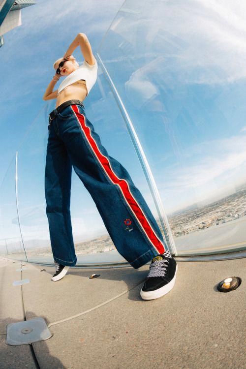 a woman standing in front of a mirror with her hands behind her head and wearing blue jeans