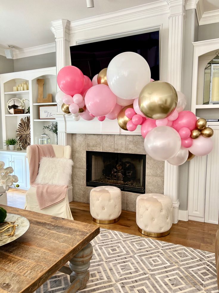 a living room filled with lots of pink and white balloons hanging from the ceiling above a fireplace