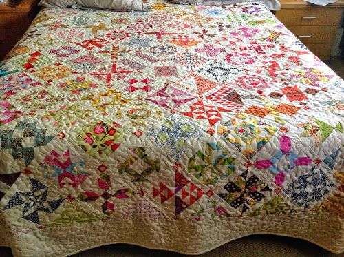 a bed with a colorful quilt on top of it next to a night stand and lamp