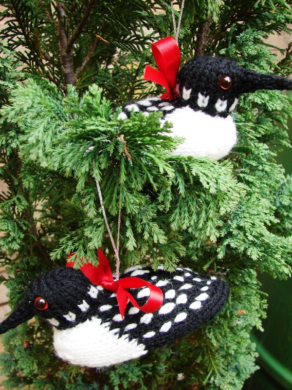 two black and white birds are hanging from a christmas tree with red bows on their heads